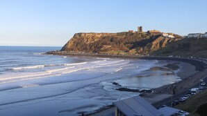 A coastal view with a cliff and a castle-like structure on top. - Apartment 6 Bay View (Scarborough)