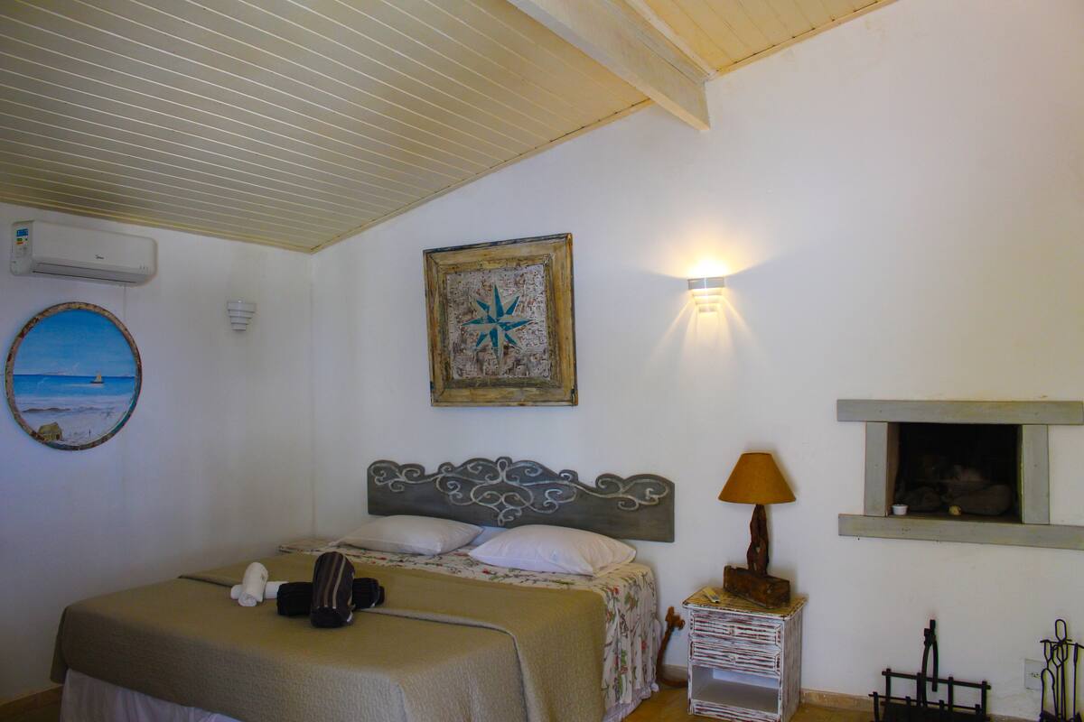 Une chambre à coucher avec un lit, un climatiseur fixé au mur, un tableau encadré, une lampe de chevet et une fenêtre donnant sur un beau paysage.