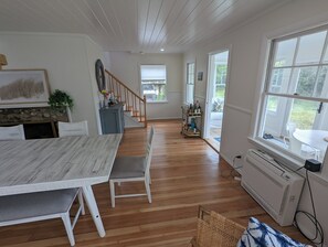 Un salón amplio con suelo de madera, una mesa de comedor con sillas, una escalera y vistas al exterior.