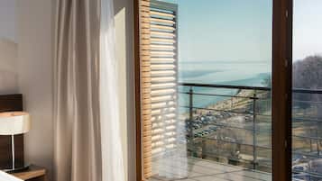 Enjoy a serene view of the water from this room's large window, featuring a comfortable bed and a convenient bedside table with a lamp.