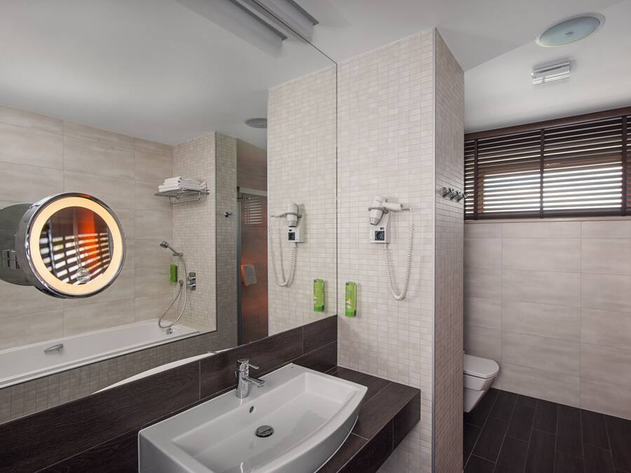 A modern bathroom with a large mirror, a sink, a toilet, and a shower area.