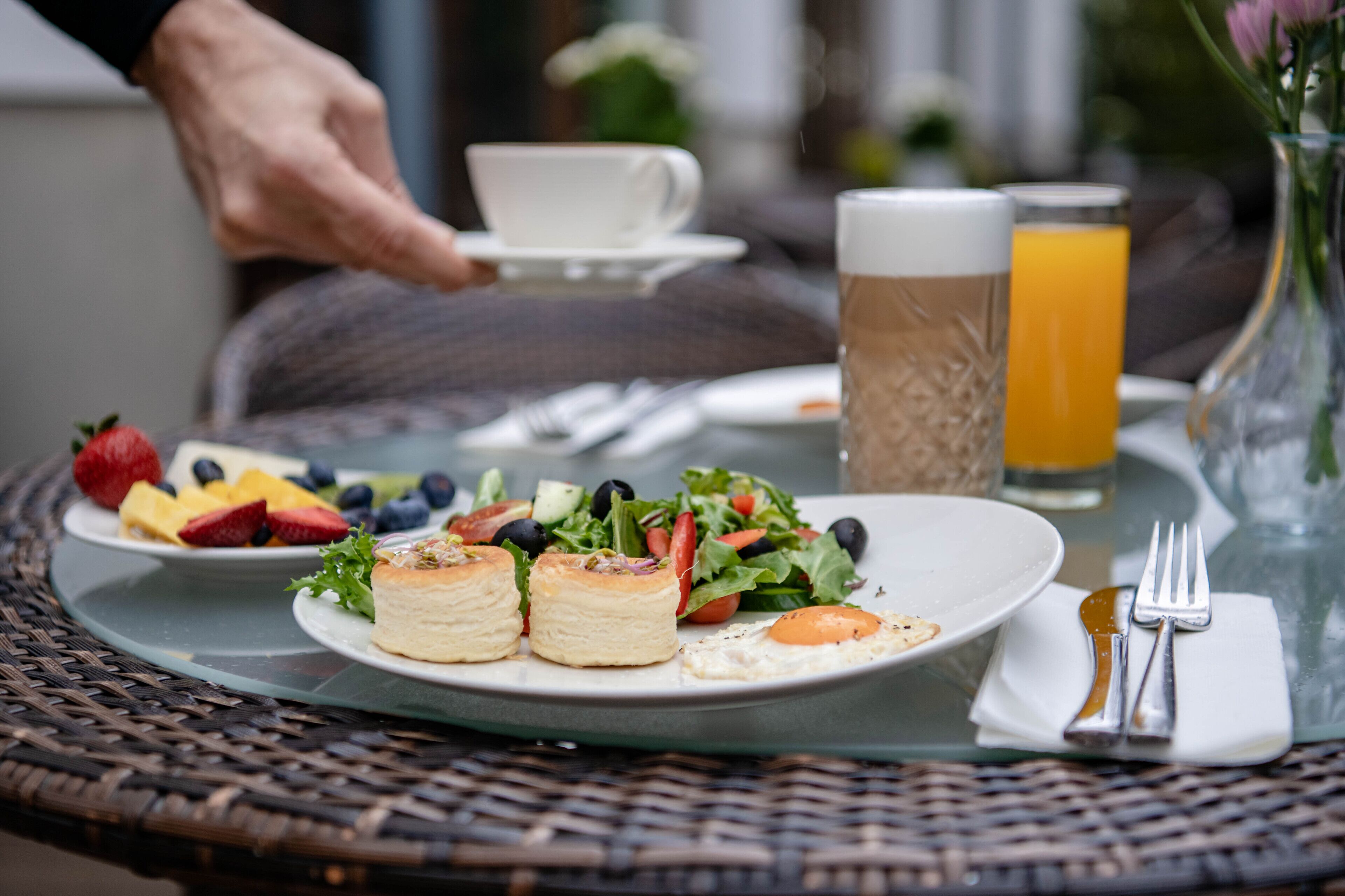 A breakfast setting with a plate of food, a glass of orange juice, and a cup of coffee on a wicker table.