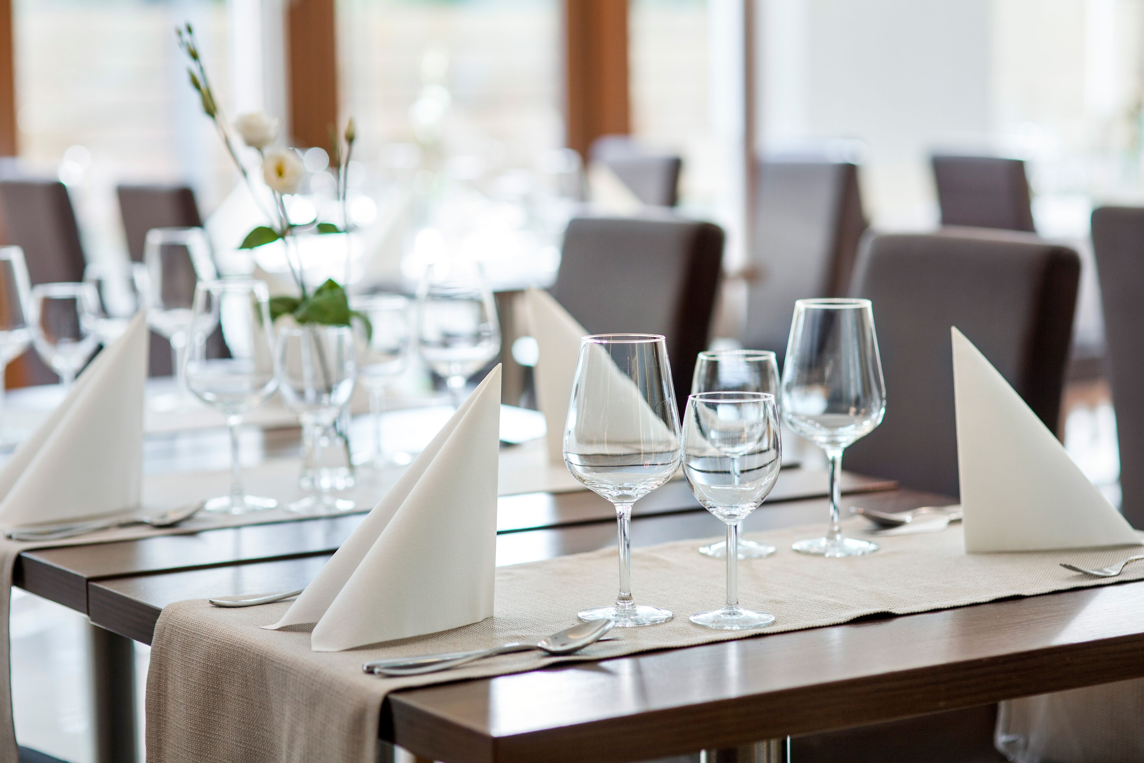 A dining table set with wine glasses, napkins, and a vase with flowers.