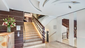 A modern hotel lobby with a wooden reception desk, a marble staircase, and a glass partition wall. - Hotel Różany Gaj - Destigo Hotels (Gdynia)