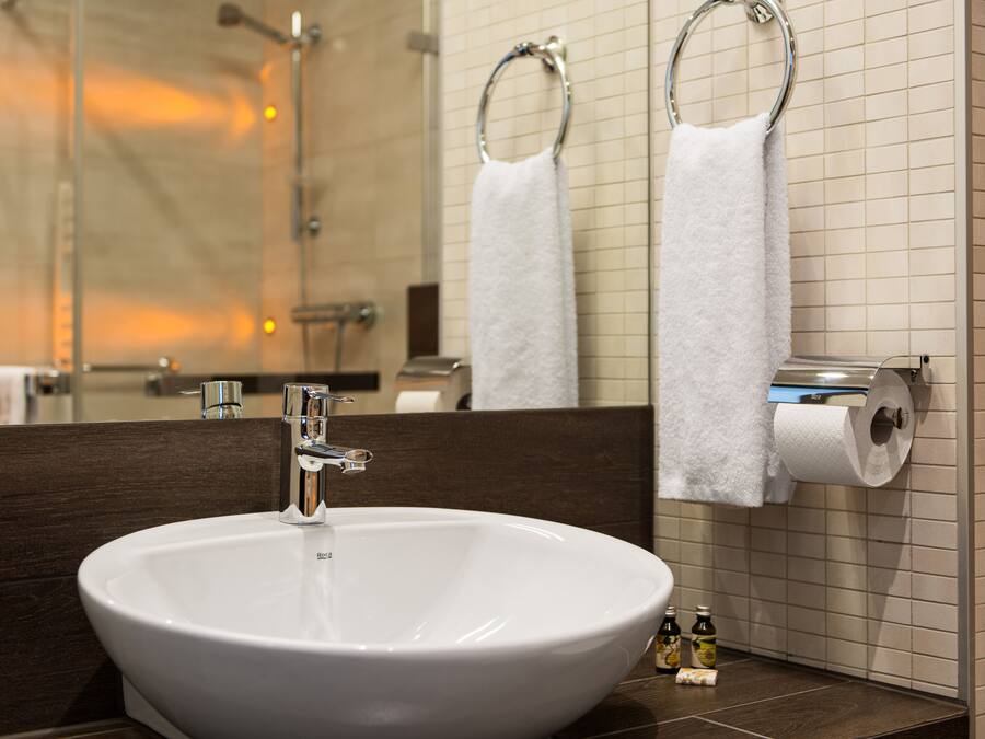 A bathroom with a large white sink, a mirror, and two towel rings.