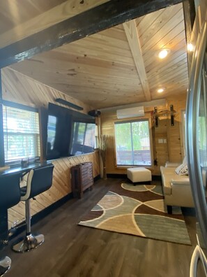 A cozy cabin interior with a wooden ceiling, a dining area with a table and chairs, a sofa, and a large window with blinds. - Beautiful Cabin Style Studio Surrounded By Nature (Cocoa)