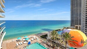 Zona de piscina d'un hotel amb gandules i ombrelles, amb vista a una platja i l'oceà.