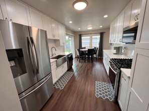 A modern kitchen with stainless steel appliances, white cabinetry, and a dining area with a table and chairs. - Remodeled SFR w/fireplace, super close to main highways and Chicago (Darien)