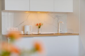 Una cocina moderna con armarios blancos, protector de encimera de mármol, cafetera y un florero con flores sobre la encimera.