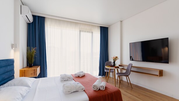 A modern hotel room with a bed, a TV, a desk, and a chair. - Next Orange Aparthotel Official (Batumi)