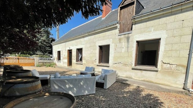 A building with a stone facade, multiple windows, and outdoor seating area with a gravel ground. - Longère Tourangelle (Bréhémont)