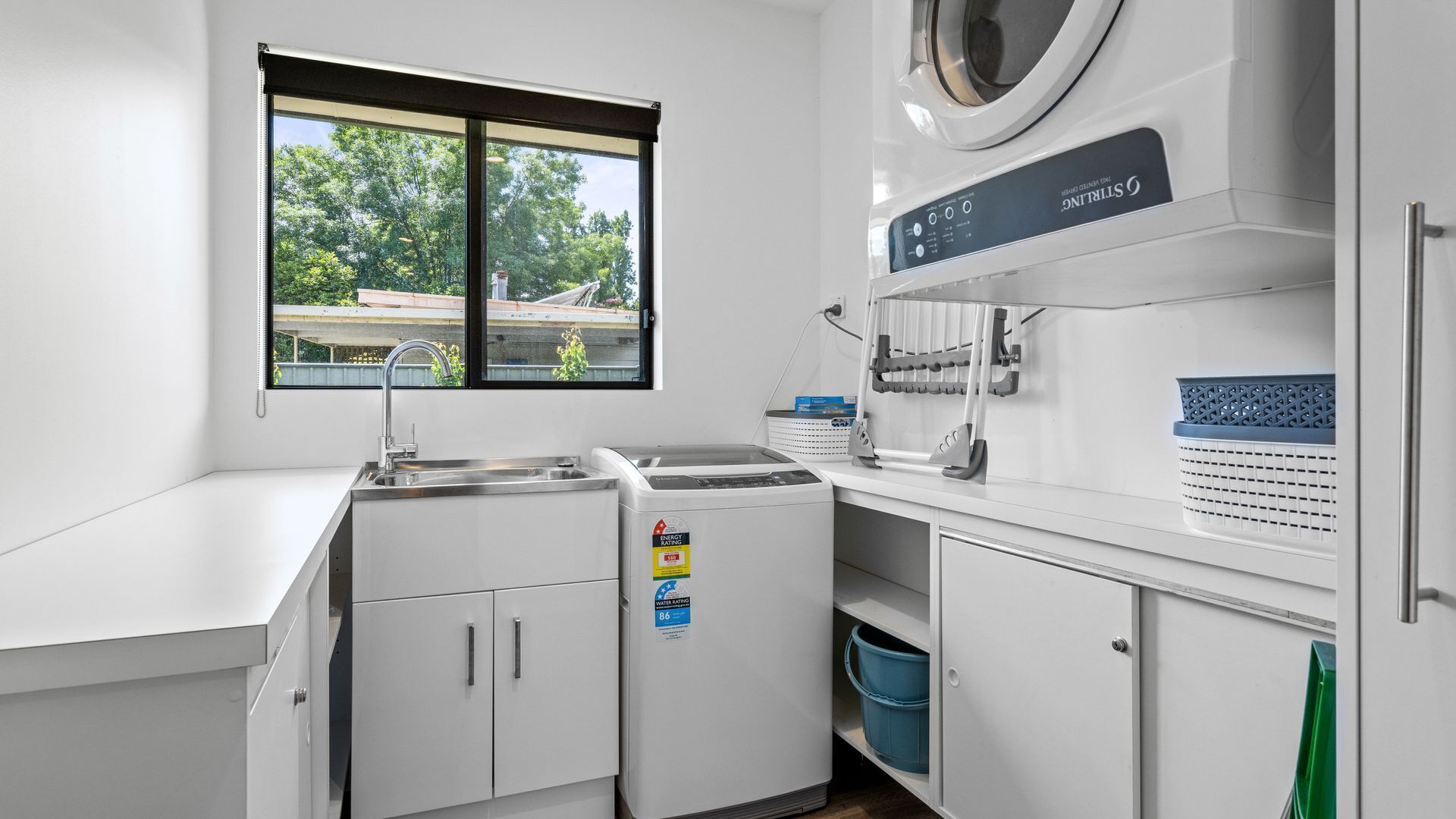 Een moderne keuken met een ingebouwde wasmachine, een spoelbak en een raam met uitzicht op groen.