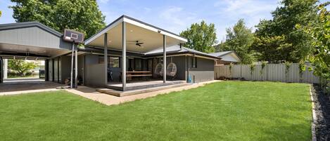A modern house with a covered patio, a basketball hoop, and a well-maintained lawn.