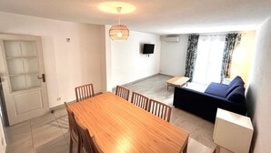 A compact living space with a wooden dining table, a sofa, and a TV mounted on the wall.