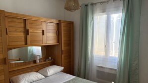 A bedroom with a wooden bed frame, a bedside table, a mirror, and a window with curtains.