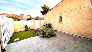 A courtyard with a wooden deck, a white fence, and a building with a beige exterior.