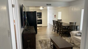 Amplia sala de estar con una mesa de comedor, sillas, un sofá y una cocina al fondo.
