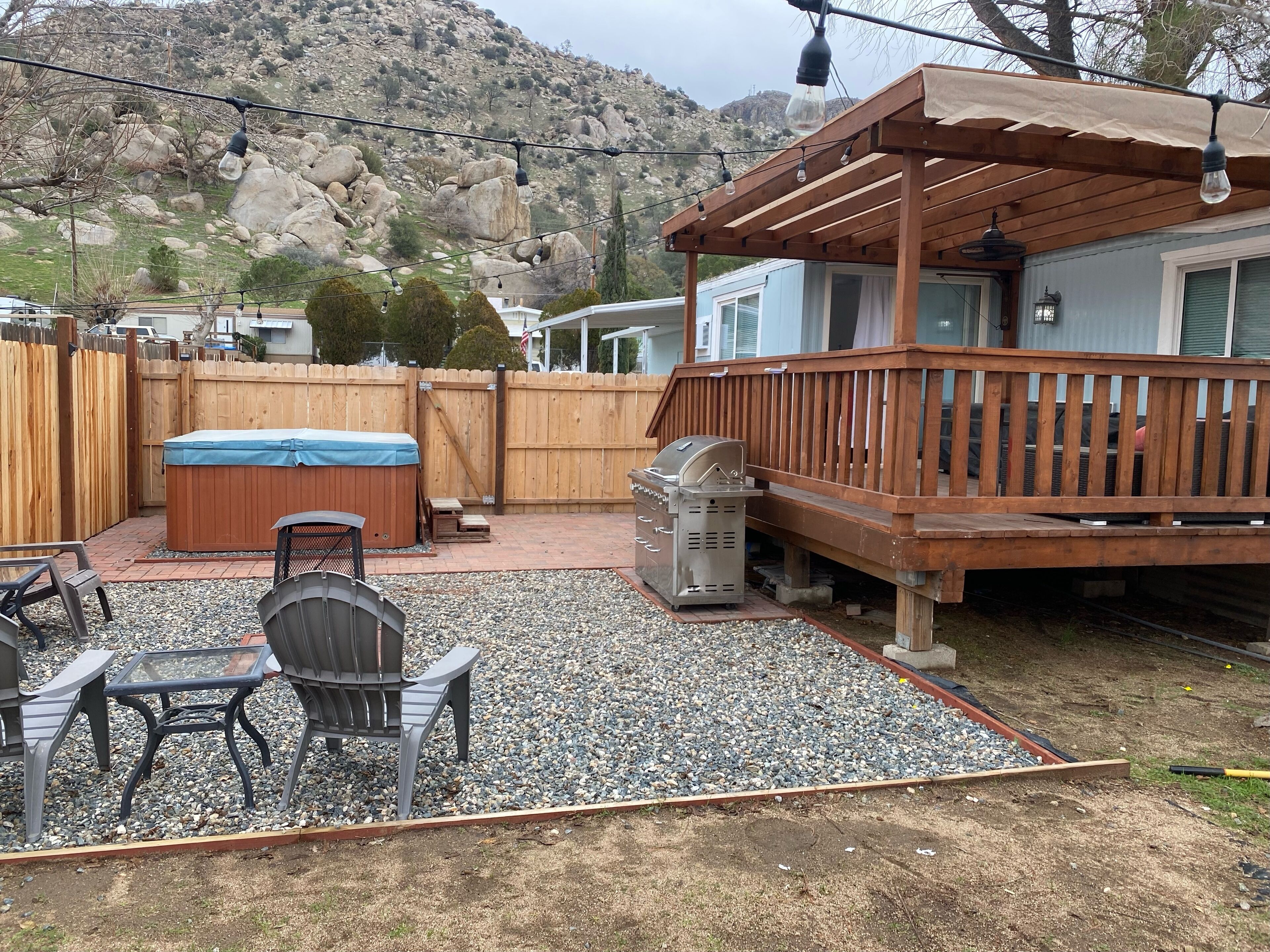 A backyard with a wooden deck, a hot tub, a grill, and a patio table with chairs.