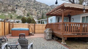 Un patio trasero con una terraza de madera, un jacuzzi, una parrilla y una mesa de patio con sillas.
