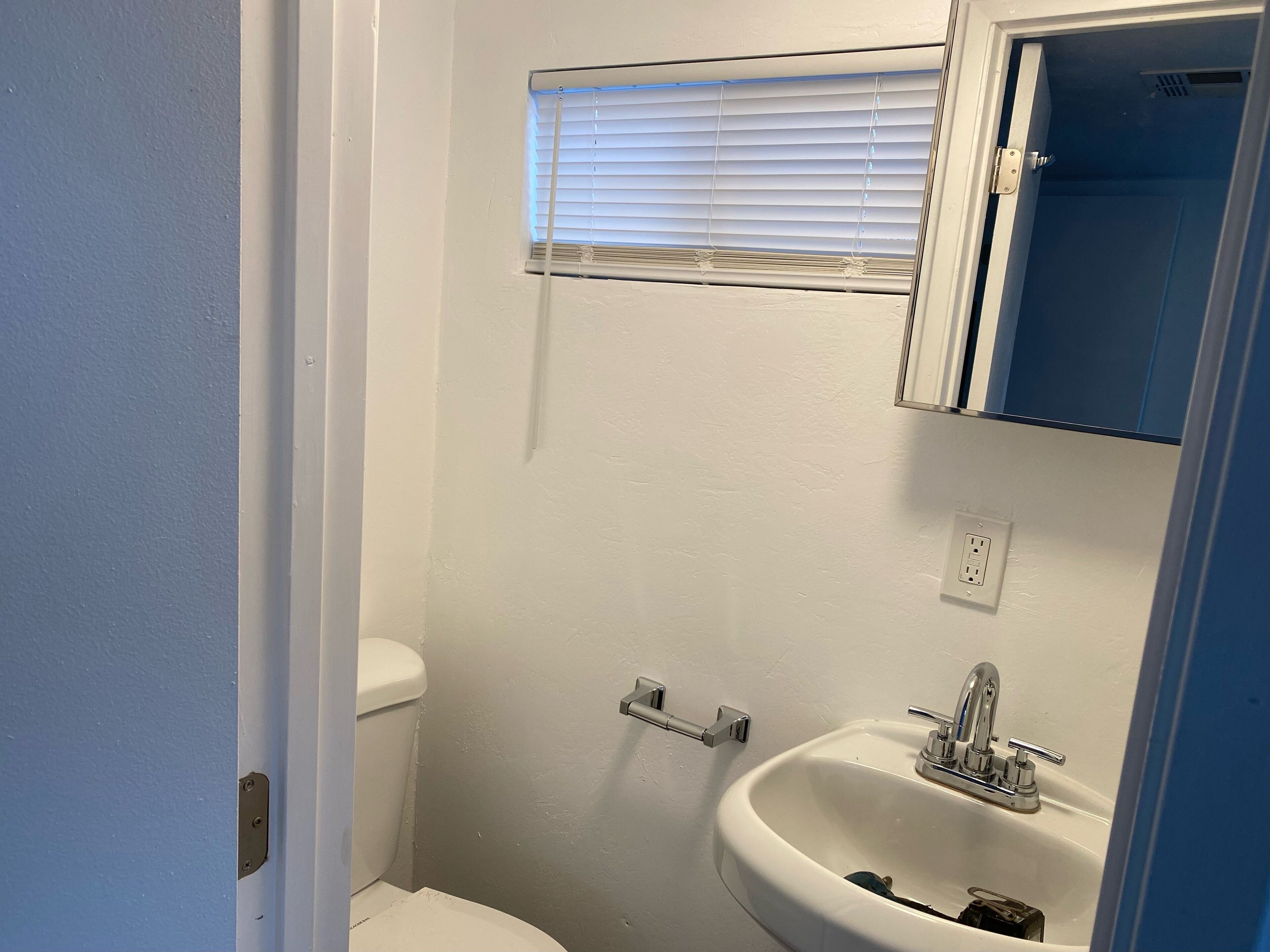 Ein kleines Badezimmer mit Toilette, Waschbecken und Fenster mit Jalousien.
