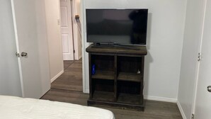 Un dormitorio con una cama, un televisor sobre un mueble de madera, una puerta y un pasillo.