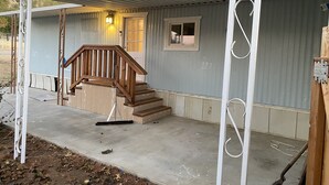 Una casa de un piso con una escalera de madera que lleva a una puerta principal, una ventana pequeña y un porche.
