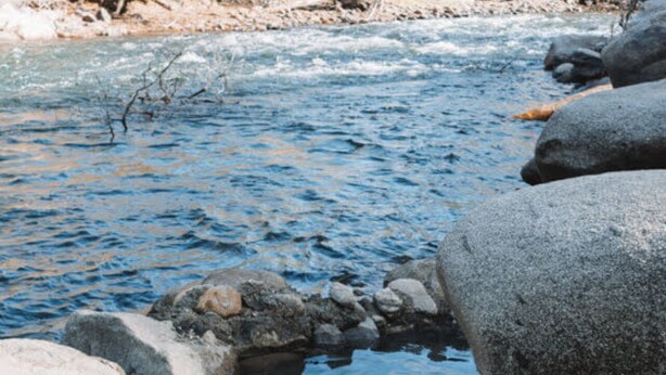 Una persona sentada junto a la orilla rocosa de un río.