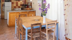 Une cuisine rustique avec des poutres en bois, une table à manger avec des chaises et un vase rempli de fleurs violettes.