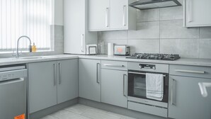 A modern kitchen with grey cabinets, a built-in oven, a gas stove, and a window with blinds. - The Whetstone - Modern 2B Apartment in Edgbaston! (Birmingham)