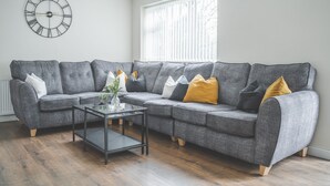 A modern living room with a grey sectional sofa, a glass coffee table, and a wall clock. - The Whetstone - Modern 2B Apartment in Edgbaston! (Birmingham)