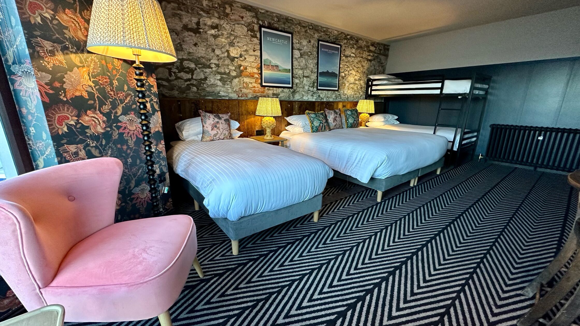 Une chambre d’hôtel avec deux lits, un mur en pierre et un sol à motifs.