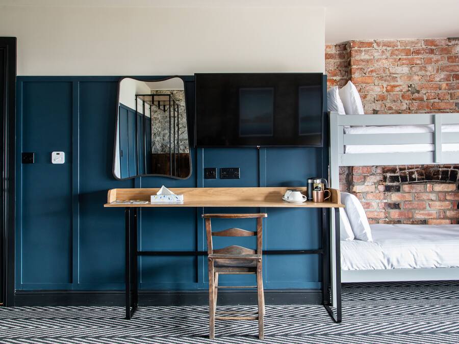 Una habitación con una cama litera, un escritorio con silla, un espejo y una pared de ladrillo.