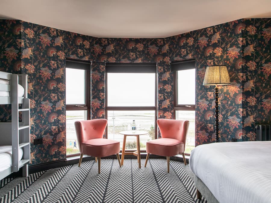 Una habitación con una cama litera, dos sillas rosas, una mesita y una lámpara.