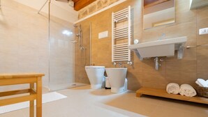 Een moderne badkamer met een douche, twee toiletten, een wastafel en een houten bankje.