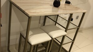 Eine kleine, moderne Küchenzeile mit einer Marmorarbeitsplatte, zwei Barhocker und einem an der Wand montierten Flachbildfernseher.