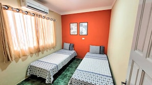 A small room with two single beds, a window with curtains, and an air conditioning unit. - House Maraca (Ipojuca)