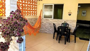 A covered patio with a tiled floor, a dining table with chairs, a hammock, and a decorative wall. - House Maraca (Ipojuca)