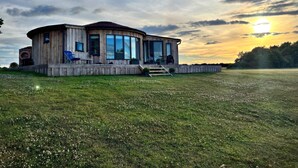 A wooden cabin with large windows, a deck, and a grassy field. - Cosy Luxury Lakeside Lodge, surrounded by amazing views and countryside. (Newark)
