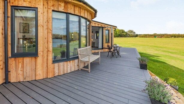 A wooden house with large windows, a deck, and a view of a green field. - Cosy Luxury Lakeside Lodge, surrounded by amazing views and countryside. (Newark)