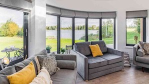 A modern living room with a grey sofa set, a coffee table, and a view of a green landscape through large windows. - Cosy Luxury Lakeside Lodge, surrounded by amazing views and countryside. (Newark)