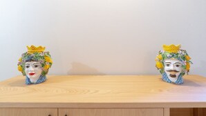 Zwei Keramikkopfskulpturen mit Kronen auf einem Holztisch vor einer schlichten Wand.