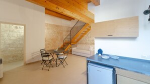 Eine moderne Küche mit Holzbalkendecke, einer Essecke mit Tisch und Stühlen, einer Treppe und einem kleinen Kühlschrank.