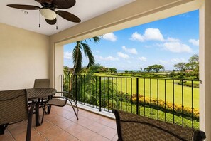 A balcony with a view of a golf course, a ceiling fan, and a table with chairs.