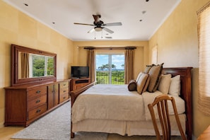 A bedroom with a bed, a TV, a dresser, and a balcony with a view.