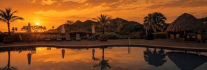 A pool reflecting a sunset with palm trees and lounge chairs.