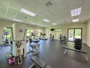 Ginásio com máquinas de cardio, equipamentos de musculação e um banco.