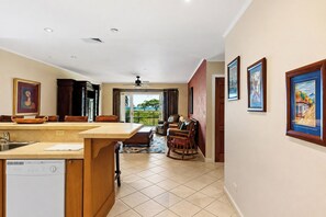 A kitchen with a dishwasher, a dining area with a table and chairs, and a living room with a sofa and a rocking chair.