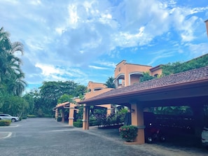 Entrada de hotel con paseos techados, palmeras y cielo despejado.