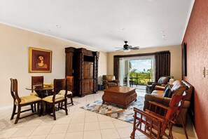 A spacious living room with a dining area, a large wooden cabinet, a ceiling fan, and a view of the outdoors through a sliding glass door.