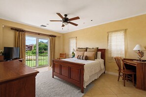A bedroom with a bed, a desk, a chair, a television, and a ceiling fan.